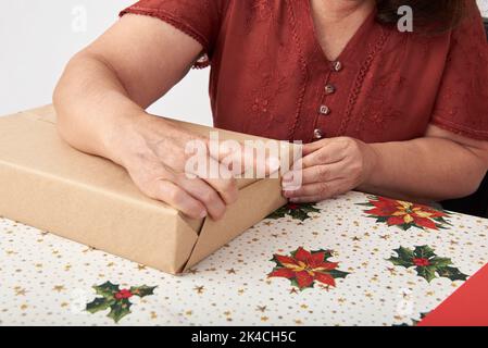 Femme adulte non reconnaissable emballant cadeaux de vacances. Design aux couleurs de Noël traditionnelles et espace de copie. Banque D'Images