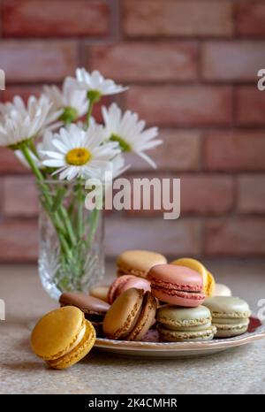 Les pâquerettes d'été font une douce vie à côté de cette assiette de macarons français croustillants Banque D'Images