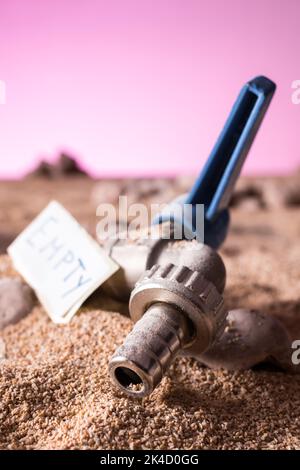 Gros plan vertical d'un robinet ouvert et sec enterré par du sable désertique avec une plante succulente contre un fond de ciel rose et sec menaçant avec un panneau vide Banque D'Images