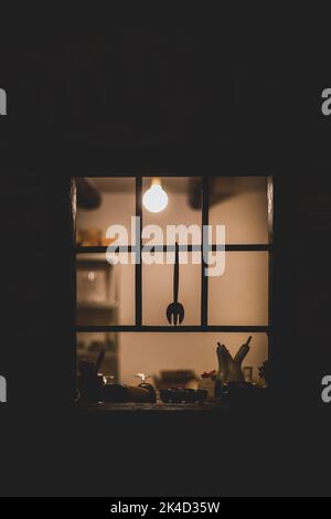 Vue verticale d'une fenêtre de cuisine de l'extérieur la nuit avec lumières allumées Banque D'Images