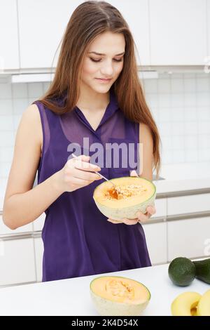 Retirer le cantaloup. Une jolie jeune femme qui retire les graines de son cantaloup dans la cuisine. Banque D'Images