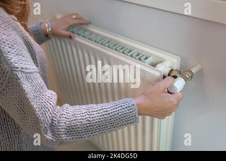 Femme ajustant la température sur radiateur de chauffage, concept de crise énergétique en Europe, augmentation des coûts dans les ménages privés pour la facture de gaz en raison de l'inflation et Banque D'Images