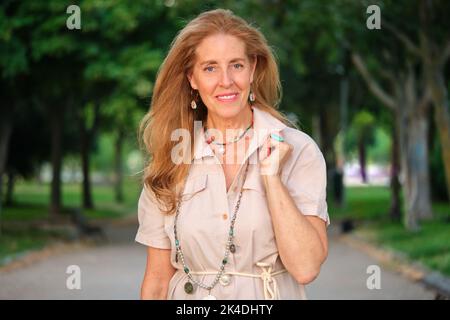 Portrait extérieur de femme mûre souriante aux yeux bleus et blond. Banque D'Images