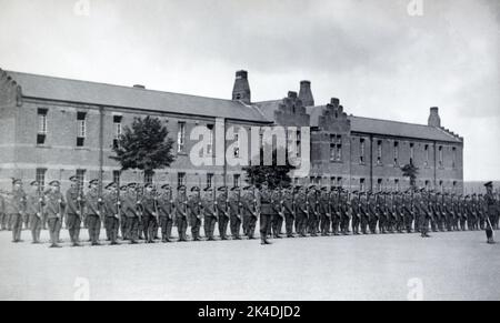 Un tableau de l'entre-deux-guerres des officiers de l'armée britannique et se solidifie sur le défilé présentant des armes pour un salut général avec les riles, à l'extérieur d'une caserne de briques. Banque D'Images