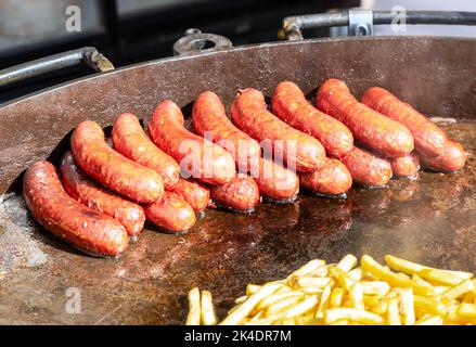 De délicieuses saucisses à base de viande sur une grande poêle en métal grillant sur des charbons chauds pour un déjeuner pique-nique Banque D'Images