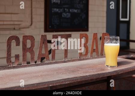 Un verre non fini de bière non filtrée sur un comptoir en fer à repasser. En arrière-plan se trouve une façade floue d'un pub. Banque D'Images