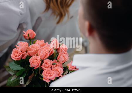 Un jeune homme tient un grand bouquet de roses roses le jour de la femme. Fleurs de rose fraîches. Banque D'Images