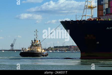 Remorqueur tirant Un gros navire à conteneurs avec Une ligne de remorquage dans le port de Southampton Docks, Royaume-Uni Banque D'Images