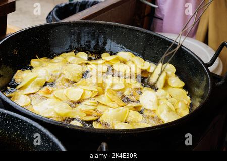 Faire frire les pommes de terre tranchées dans l'huile et remuer avec une cuillère à créneaux Banque D'Images