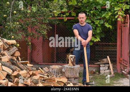 un homme avec une hache se tient à côté d'un tas de bois de chauffage haché. Banque D'Images