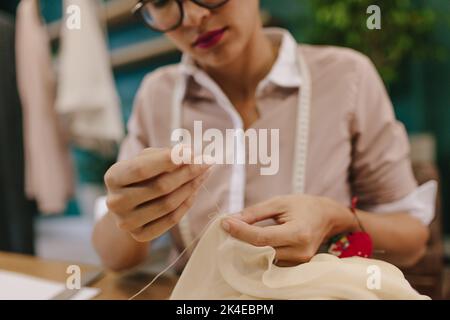 Gros plan de femme mains couture robe de designer à son lieu de travail. Femme de mode travaillant dans son studio. Les mains du couturier font du travail à main sur le dre Banque D'Images