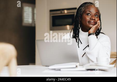 Femme d'affaires sénior regardant loin avec soin tout en travaillant sur un ordinateur portable à la maison. Femme d'affaires mature qui fait du travail indépendant en ligne dans son bureau à domicile. Banque D'Images