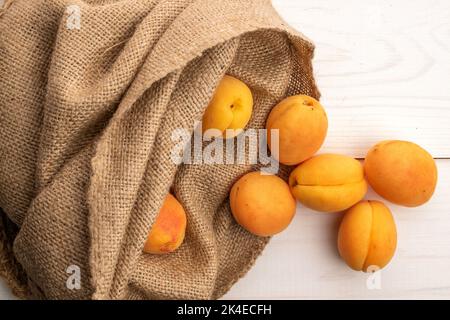 Plusieurs abricots jaunes d'ananas biologiques dans un sac de jute, gros plan, sur une table en bois blanc, vue de dessus. Banque D'Images