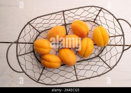 Plusieurs abricots jaunes d'ananas biologiques dans un panier en métal, gros plan, sur une table en bois blanc, vue de dessus. Banque D'Images