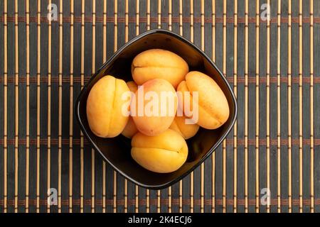 Plusieurs abricots jaunes d'ananas dans une assiette, gros plan, sur un tapis de bambou, vue de dessus. Banque D'Images