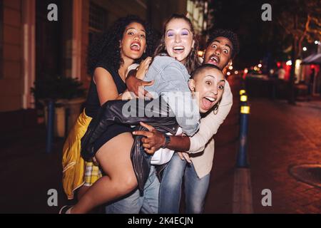 Des amis fous s'amusent ensemble en ville. Les jeunes multiculturels crient avec joie tout en se traînant ensemble à l'extérieur la nuit. Groupe de frie Banque D'Images