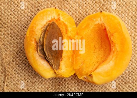 Un abricot jaune ananas coupé en deux, macro, sur le tissu jute, vue du dessus. Banque D'Images