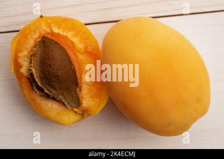 Un abricot jaune ananas et un demi avec un os, gros plan, sur une table en bois blanc, vue du dessus. Banque D'Images