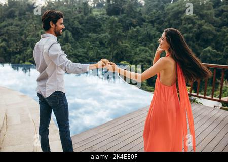 Portrait d'un couple caucasien dansant près de la piscine. Un jeune homme et une jeune femme s'amusent au bord de la piscine d'une station de vacances dans la nature. Banque D'Images