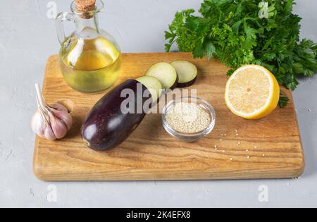 Ingrédients pour l'apéritif Baba ganoush d'aubergines cuites au four, persil, sésame, citron, ail et huile d'olive sur bois sur fond gris. Arabe a Banque D'Images