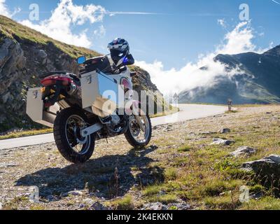Une moto d'aventure avec de grands boîtiers en aluminium est garée sur un col de montagne dans les Alpes européennes. Vue arrière, vue en angle bas Banque D'Images
