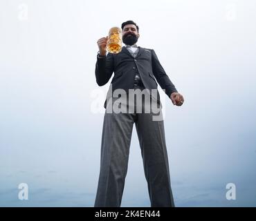 Drôle de barbu hipster homme tient la bière artisanale sur fond de ciel nature. Pleine longueur, grand angle, bannière, espace de copie. Banque D'Images