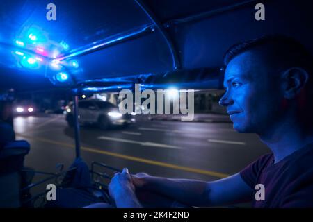 Homme en train de profiter d'une promenade en tuk tuk la nuit. Portrait du touriste en taxi. Bangkok, Thaïlande Banque D'Images