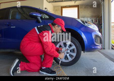 Photo d'un mécanicien dans son atelier qui, avec un tournevis pneumatique, désassemble la roue d'une voiture reposant sur des tréteaux. Travaux de réparation de voitures Banque D'Images