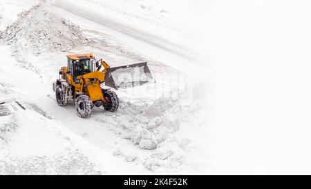 Déneigement. Le tracteur se dégage après de fortes chutes de neige. Un gros tracteur orange élimine la neige de la route et dégage le trottoir. Nettoyage des routes Banque D'Images