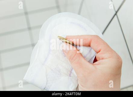 Concept de pauvreté d'hygiène, jeune femme tenant une fois bloc menstruel et pièces en main dans la salle de bains à la maison. Ne peuvent pas se permettre de nouveaux. Banque D'Images