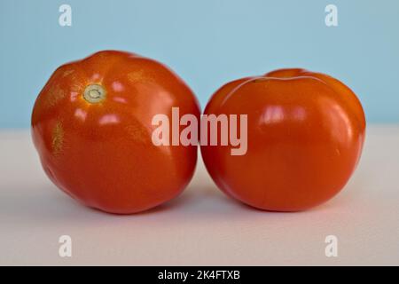 deux tomates rouges sur une surface blanche sur fond bleu clair Banque D'Images
