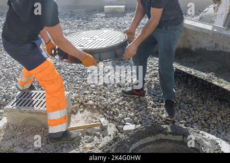 La trappe d'égout en fonte étant installée sur une base en béton dans le cadre de l'installation d'un puits d'égout dans le sol Banque D'Images