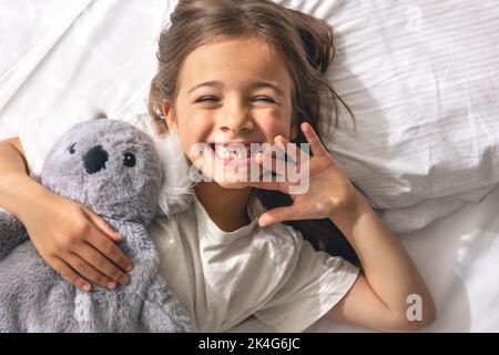 Petite fille mignonne avec son jouet doux préféré au lit le matin. Banque D'Images