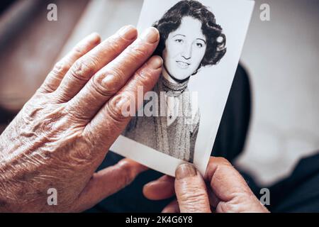 VERS 1970 : mains de femmes âgées tenant une photo vintage, en noir et blanc de la jeune femme. Concept de passage du temps Banque D'Images