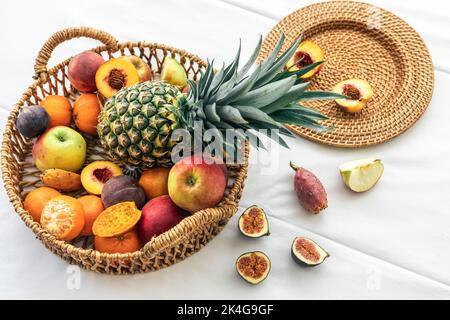 Ananas et autres fruits exotiques dans un panier en osier sur fond blanc. Banque D'Images