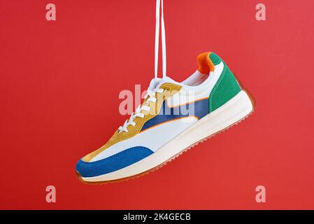 Baskets tendance suspendues sur fond rouge. Chaussures de sport élégantes et décontractées. Design minimaliste et créatif avec chaussures Banque D'Images