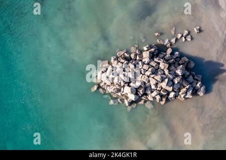 Vue aérienne directement au-dessus d'un tas de rochers utilisés pour réparer les défenses côtières et les murs de mer d'une carrière et dans l'océan sur une plage de Cornouailles Banque D'Images