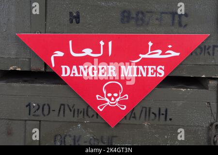 Rouge avertissement champ de mines arabe/anglais - danger Mines. Crâne blanc et crossones sur un rouge. Sur des caisses vertes de l'armée. Texte en russe : type de l'unité de mesure Banque D'Images