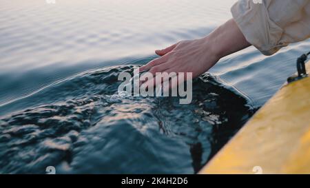 Personne plonge la main dans l'eau calme de la rivière assis dans le bateau jaune. L'homme aime le camping et la voile sur le bateau. Guy fait des vagues sur l'eau avec la main Banque D'Images