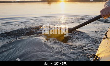 Une personne inconnue navigue en kayak à l'aide d'une paddle jaune sur un lac forestier. Les gouttelettes tombent dans l'eau claire au coucher du soleil. Anonyme fait des vagues avec paddle closeup Banque D'Images