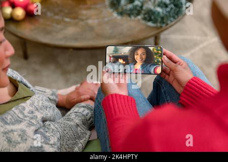 Joyeux couple divers faisant appel vidéo de noël smartphone avec couple biracial souriant. noël, festivité et technologie de communication. Banque D'Images