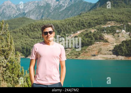 Portrait de l'homme souriant dans des lunettes de soleil debout près du lac des montagnes sur le fond. Positif jeune homme voyageant sur le lac bleu en plein air voyage aventure Banque D'Images
