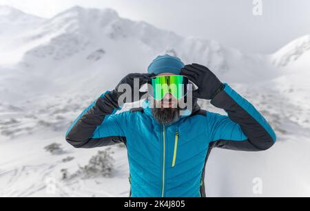 Homme mettant des lunettes de ski, se préparant pour le ski d'hiver dans les montagnes enneigées. Banque D'Images