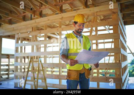 Ingénieur de construction ou architecte avec des plans-plans visiter et damier le site de construction écologique d'une maison en bois. Banque D'Images