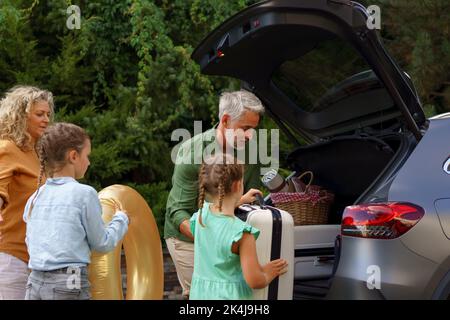 Famille avec de petits enfants qui chargent la voiture et qui attendent de charger la voiture avant de partir en vacances. Banque D'Images