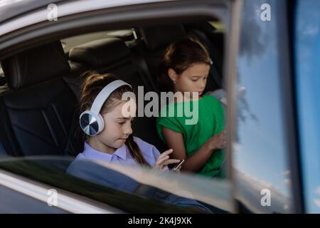 Petites sœurs assises en voiture, écoutant de la musique et attendant un voyage en voiture. Banque D'Images