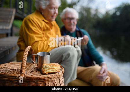 Heureux couple senior ayant pique-nique et se reposant près du lac après la marche. Banque D'Images