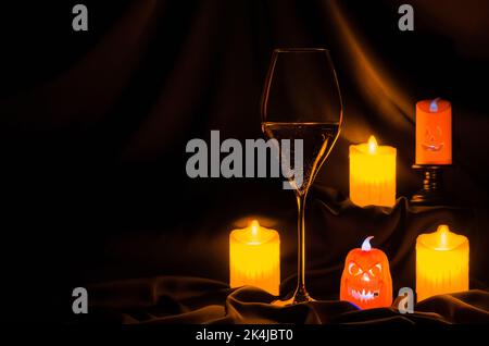 Un verre de vin blanc avec une petite lanterne d'halloween et une bougie floue sur fond de tissu foncé. Concept dîner d'Halloween. Banque D'Images
