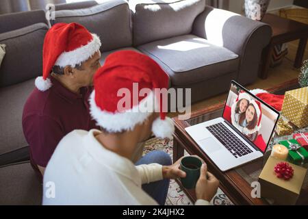 Père et fils d'oiseaux faisant passer un appel vidéo de noël avec une mère et une fille souriantes. noël, fête et technologie de communication. Banque D'Images