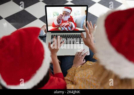 La mère et la fille qui font l'ordinateur portable appel vidéo de noël avec un homme âgé habillé comme le père noël. noël, festivité et technolog de communication Banque D'Images